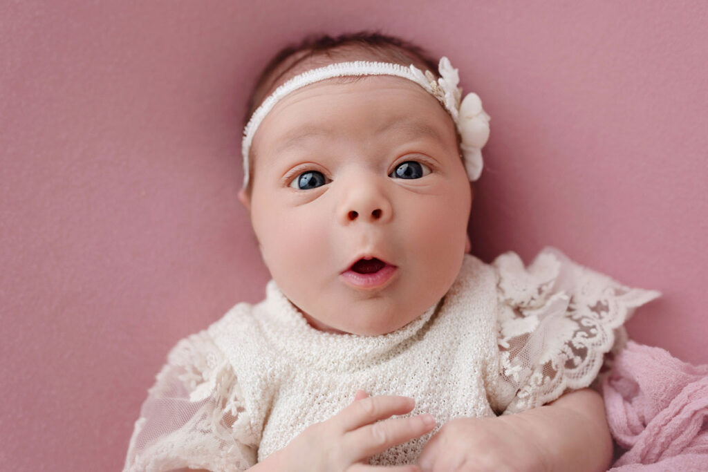 Zwei Wochen altes Baby mit Haarband schaut neugierig in die Kamera