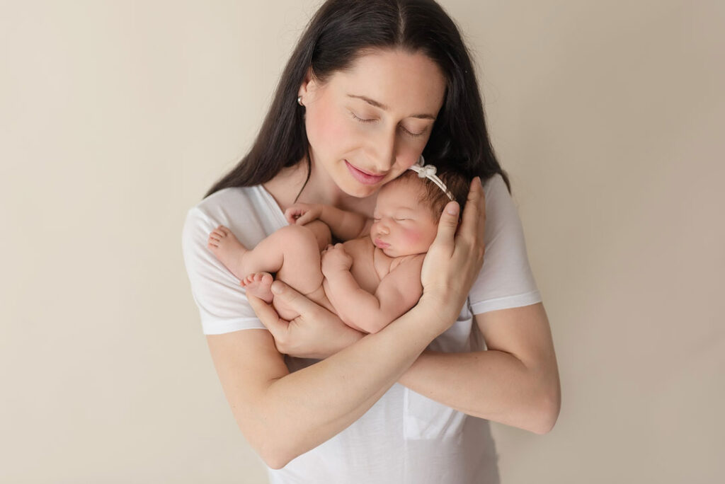 Mama hält ihr neugeborenes Baby zärtlich im Arm, Neugeborenenfotos Wien